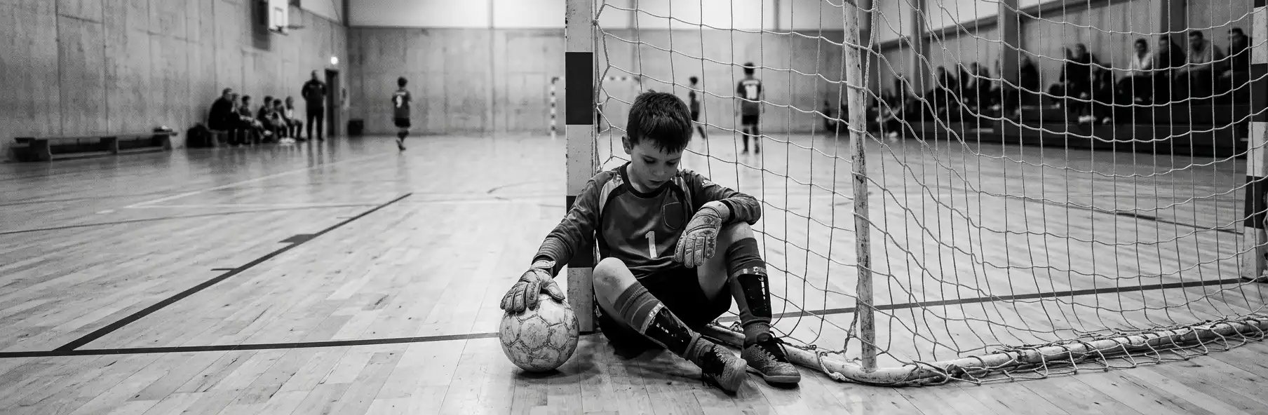 Young futsal goalkeeper sitting inside the goal looking at the floor after conceding