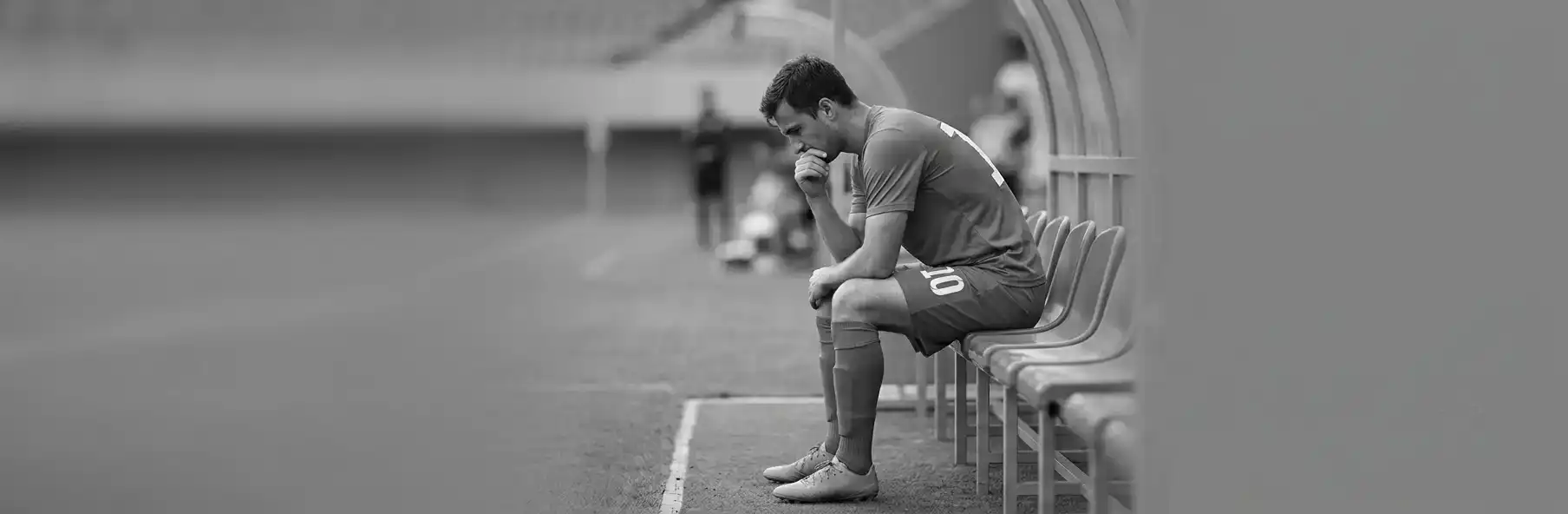 Football player sitting on the substitutes' bench visibly frustrated during a match