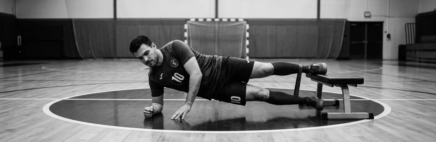 Futsal player doing the Copenhagen adductor exercise on a sports hall bench with a teammate's support