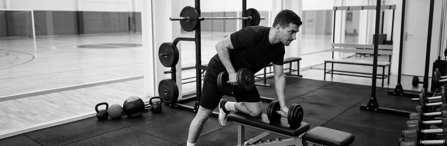 Futsal player doing a barbell squat in a small gym wearing club kit